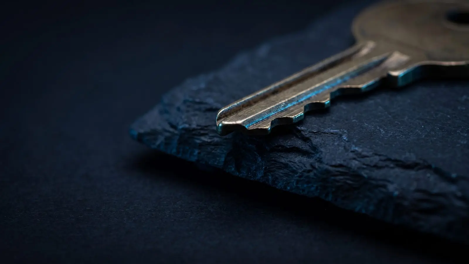Close-up of the cut teeth of a brass key on dark slate.