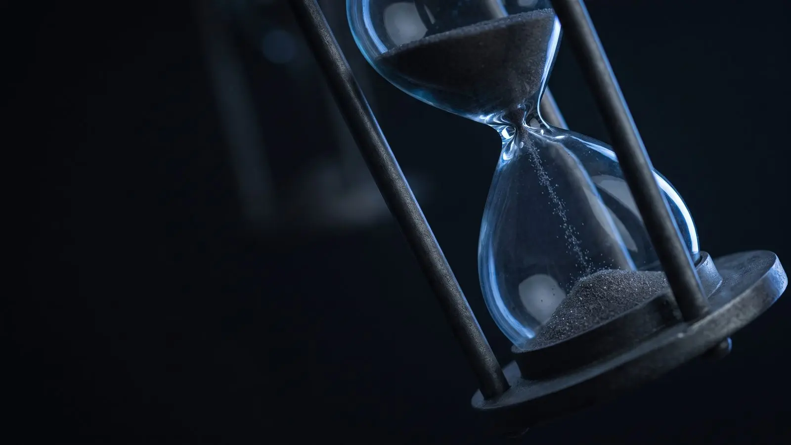 An hourglass with sand falling, lit from one side in blue.