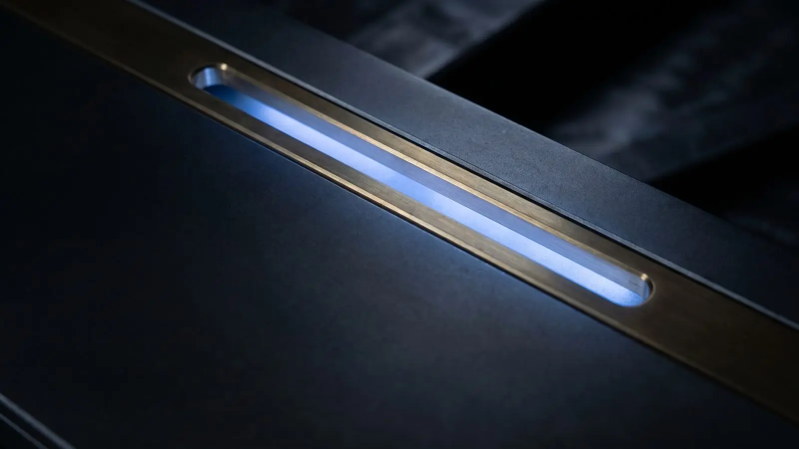 A narrow brass slot in a dark metal door with blue light spilling through.